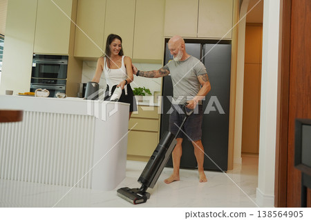 Man with woman vacuuming in modern sunlight kitchen. Man with woman vacuuming in modern sunlight kitchen. 138564905