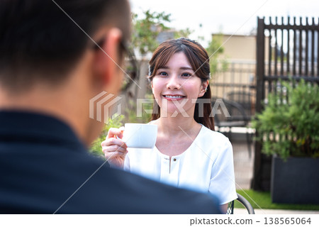 A lifestyle featuring a man and a woman enjoying tea time on a bright terrace. 138565064