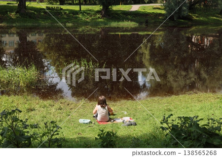Calm woman unwinding next to tranquil river during sunny afternoon Calm woman unwinding next to tranquil river during sunny afternoon 138565268