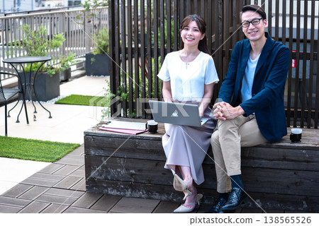 A young man and woman enjoying a conversation over coffee outdoors while working remotely. A young man and woman enjoying a conversation over coffee outdoors while working remotely. 138565526