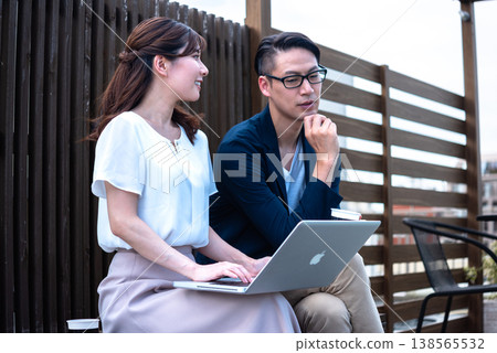 A young man and woman enjoying a conversation over coffee outdoors while working remotely. A young man and woman enjoying a conversation over coffee outdoors while working remotely. 138565532