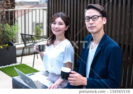 A young man and woman enjoying a conversation over coffee outdoors while working remotely. A young man and woman enjoying a conversation over coffee outdoors while working remotely. 138565539