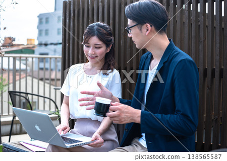 A young man and woman enjoying a conversation over coffee outdoors while working remotely. 138565587