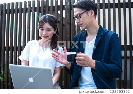 A young man and woman enjoying a conversation over coffee outdoors while working remotely. A young man and woman enjoying a conversation over coffee outdoors while working remotely. 138565592