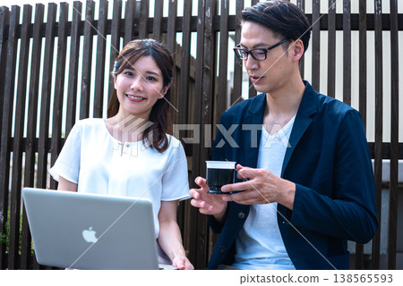 A young man and woman enjoying a conversation over coffee outdoors while working remotely. A young man and woman enjoying a conversation over coffee outdoors while working remotely. 138565593