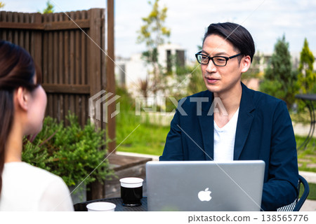 Businessmen and women having a meeting on a terrace, gathered around laptops. 138565776
