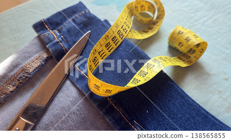 Closeup of denim jeans with scissors and coiled yellow measuring tape for tailoring background and clothing repair design 138565855