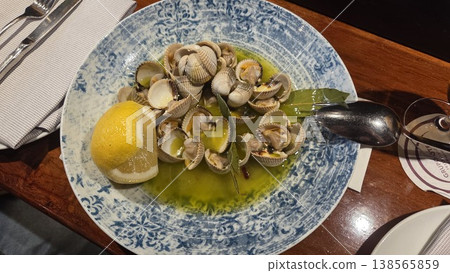 Bowl of garlic butter cockles with lemon on decorative blue plate for spanish tapas sharing platter and seafood appetizer presentation. Cockle, Cardiidae Bowl of garlic butter cockles with lemon on decorative blue plate for spanish tapas sharing platter and seafood appetizer presentation. Cockle, Cardiidae 138565859