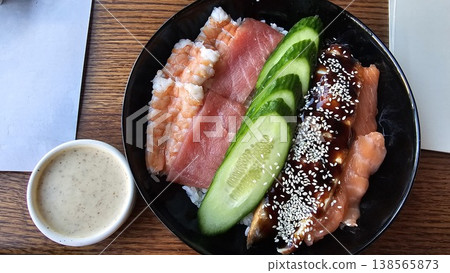 Poke bowl with salmon tuna eel shrimp rice served on black plate eating with chopsticks Asian cuisine healthy omega food 138565873