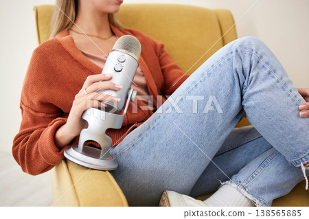 Microphone, closeup and woman hosting a podcast on a chair by a wall in her modern home. Radio, broadcast and young female person hosting a journalism talk show in a recording space at her house. 138565885
