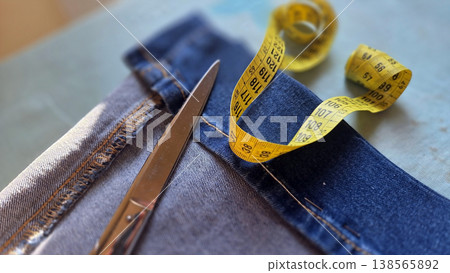 Denim sewing scene with scissors and yellow measuring tape on blue fabric and jeans for tailor background and textile design 138565892