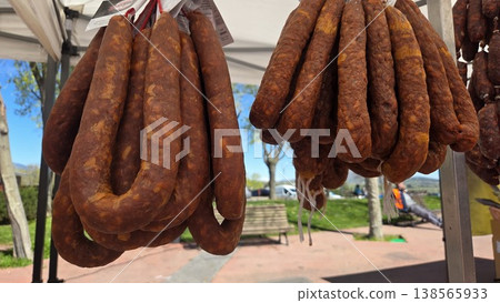 Long cured chorizo links hanging in bunches at an outdoor spanish farmers market for deli display background and traditional food banner Long cured chorizo links hanging in bunches at an outdoor spanish farmers market for deli display background and traditional food banner 138565933