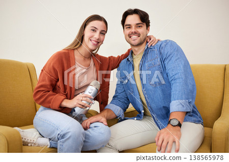 Portrait, microphone and podcast with a couple on a sofa in the living room of their home together. Smile, radio or talkshow with a happy young man and woman in their house for live streaming 138565978