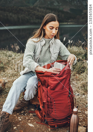 Woman, hiking and packing backpack in nature with tablet, check and thinking by lake, mountain or outdoor. Girl, luggage and trekking with bad, technology and ideas on adventure in countryside 138565984