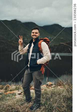 Happy man, portrait and peace sign on mountain for hiking, travel or outdoor backpacking in nature Male person or hiker smile with backpack for trekking, journey or adventure in happiness by the lake 138566236