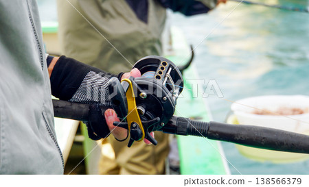 The hands of a man wearing gloves, gripping a fishing rod on a boat. The hands of a man wearing gloves, gripping a fishing rod on a boat. 138566379