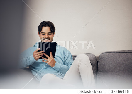 Happy man, tablet and relax on sofa for social media, communication or entertainment in living room at home. Male person, smile and lying on lounge couch with technology for online streaming at house 138566416