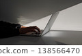 someone typing on their laptop, with the hand and computer screen visible, sitting at an all-white table, with a shadow falling across it from above 138566470