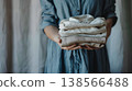 woman in a blue dress holding neatly folded and stacked , with the focus on her hands and a shirt peeking out from behind, in soft lighting and a natural look 138566488