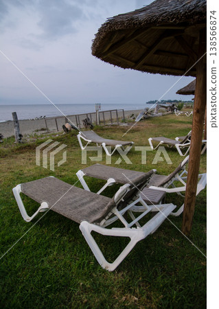 Thatched-roof parasols and beach beds line the coast at dawn on the French island of Corsica in the Mediterranean Sea. Thatched-roof parasols and beach beds line the coast at dawn on the French island of Corsica in the Mediterranean Sea. 138566874
