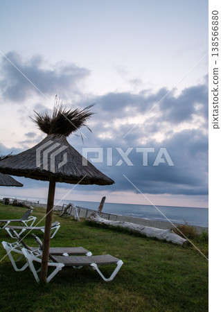 Thatched-roof parasols and beach beds line the coast at dawn on the French island of Corsica in the Mediterranean Sea. Thatched-roof parasols and beach beds line the coast at dawn on the French island of Corsica in the Mediterranean Sea. 138566880