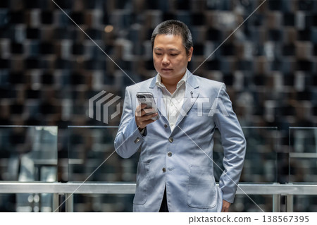 A confident businessman checks his smartphone for messages. Modern communication and connection define his daily life. 138567395
