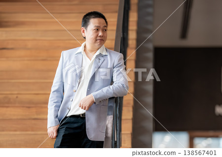 Confident Business Professional, A confident businessman stands casually by the staircase, showing calm authority and professional success. Confident Business Professional, A confident businessman stands casually by the staircase, showing calm authority and professional success. 138567401