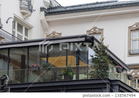 Modern building facade with an elegant glass terrace, featuring festive lights and a Christmas tree, creating a cozy urban holiday atmosphere 138567494