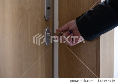 Adult hand skillfully inserting bright metal key into secure modern cylinder lock on a sturdy wooden entrance door, signifying essential property access and robust home security for residents 138567516