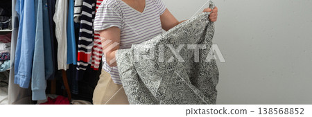 A 53-year-old woman is changing bed linen in her bedroom. She is focused on arranging new sheets while clothes hang behind her. The room is neat and well organized, banner A 53-year-old woman is changing bed linen in her bedroom. She is focused on arranging new sheets while clothes hang behind her. The room is neat and well organized, banner 138568852