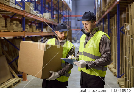 Warehouse workers doing inventory with clipboard and box in storage aisle 138568940