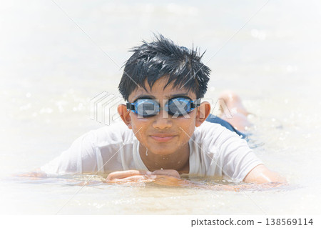 A boy's shining smile and the splashes of water on a midsummer beach. 138569114