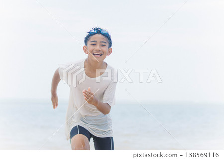 一個活潑的男孩在沙灘上奔跑，沐浴在清爽的夏日陽光下。 138569116