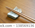一張木紋桌上擺放著一個帶有貓咪圖案的白色陶瓷筷架和一雙木製筷子。 138569136
