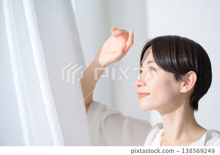 A Japanese woman basking in the sunlight streaming through a window. 138569249