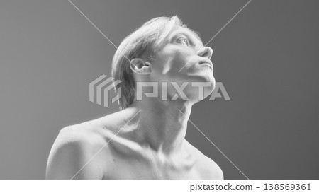 High contrast portrait of young man with upward pose in minimal studio lighting. High contrast portrait of young man with upward pose in minimal studio lighting. 138569361