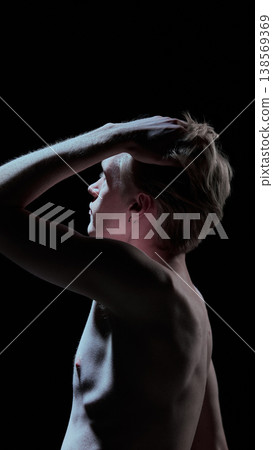 Young man touching hair in dramatic studio light with clean minimal background Young man touching hair in dramatic studio light with clean minimal background 138569369