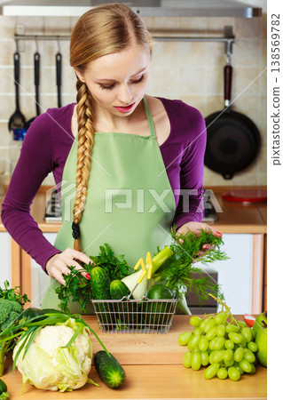 Woman in kitchen having vegetables holding shopping basket 138569782