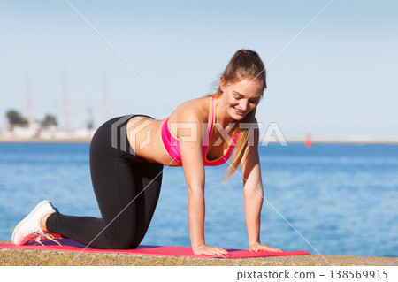 Woman doing sports exercises outdoors by seaside Woman doing sports exercises outdoors by seaside 138569915