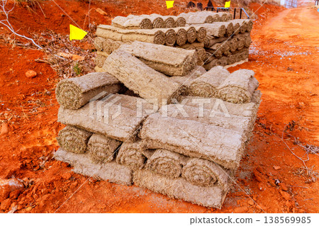 Rolls of natural material are neatly stacked beside dirt path in rural area Rolls of natural material are neatly stacked beside dirt path in rural area 138569985