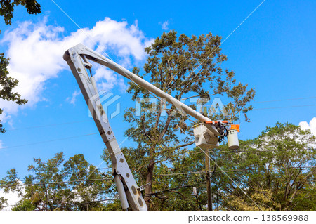 Workers use bucket truck to fix power lines after hurricane amid trees in residential area. 138569988