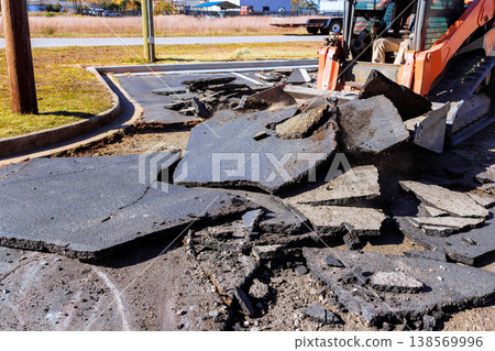 Construction work is in progress as skid steer machine breaks part cracked asphalt in parking lot Construction work is in progress as skid steer machine breaks part cracked asphalt in parking lot 138569996