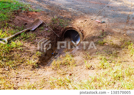 Small pipe lets water flow into cleaning drainage trench dirt path nearby, soil Small pipe lets water flow into cleaning drainage trench dirt path nearby, soil 138570005
