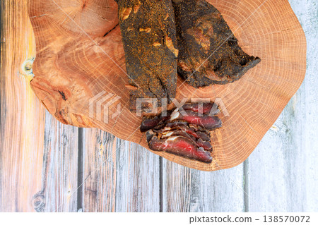 Slicing dried beef meat on wooden board in kitchen setting rustic decor. Slicing dried beef meat on wooden board in kitchen setting rustic decor. 138570072