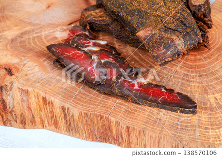 Beef jerky is cut into slices placed on wooden board with more whole cured beef Beef jerky is cut into slices placed on wooden board with more whole cured beef 138570106