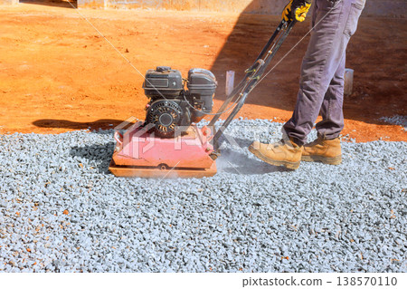 Worker operates machine gravel compactor to compress gravel on construction site Worker operates machine gravel compactor to compress gravel on construction site 138570110