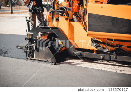Asphalt paving large machine is laying fresh asphalt on road while workers oversee process 138570117