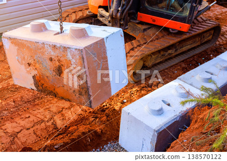 Construction work is underway as heavy machinery lifts concrete block to place it on retaining walls at building site. 138570122