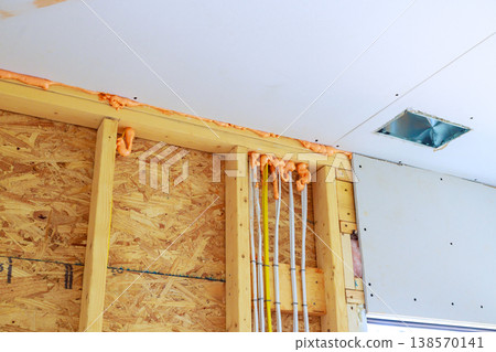 Workers are installing fire fighting foam insulation along walls with electrical pipes in construction area. 138570141