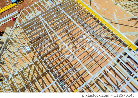 Workers install wooden beams at construction site during roof trusses tools materials are scattered around. Workers install wooden beams at construction site during roof trusses tools materials are scattered around. 138570145